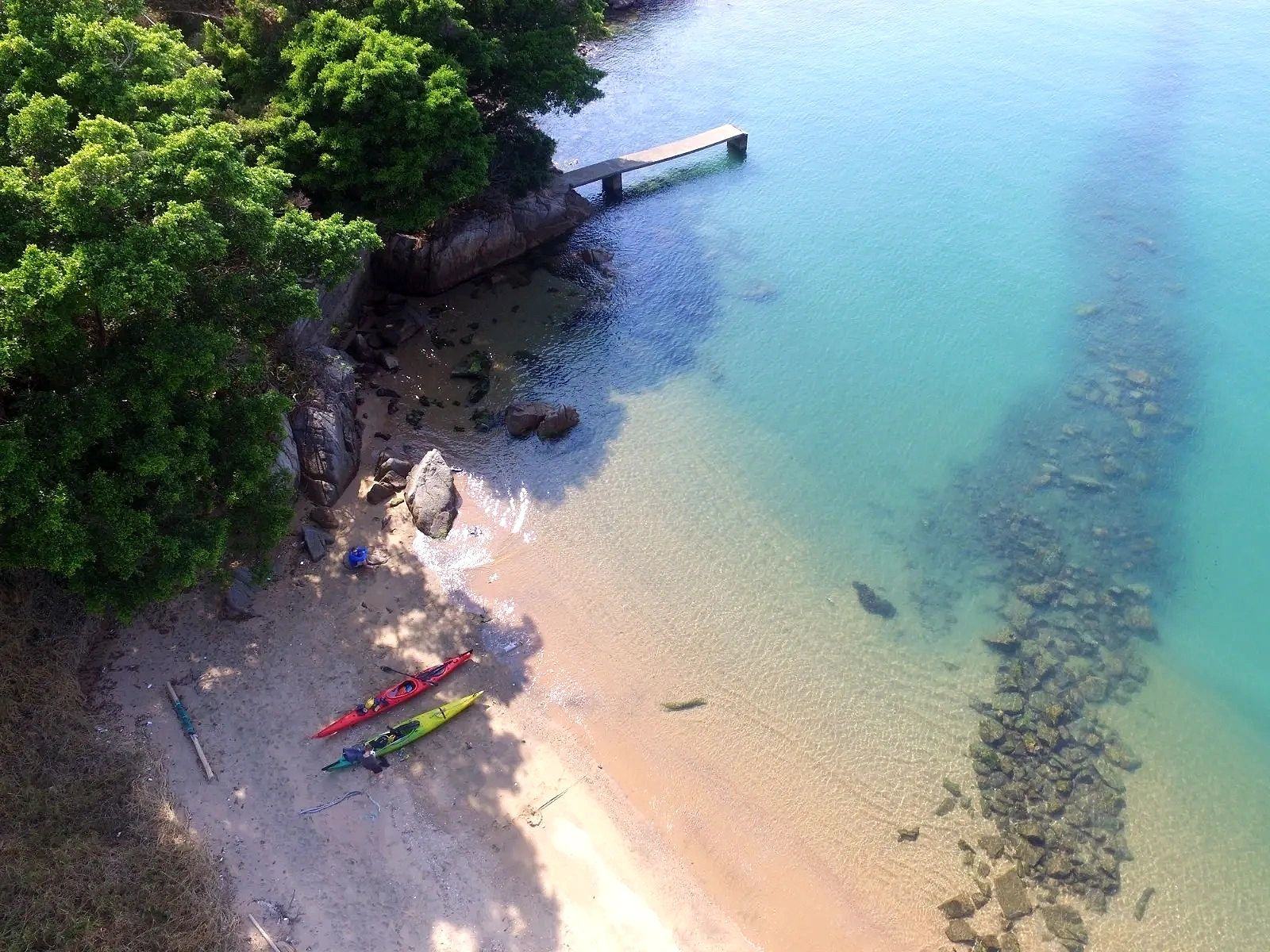 Sea kayaks pulled up on a turquoise Hong Kong beach, seen from above