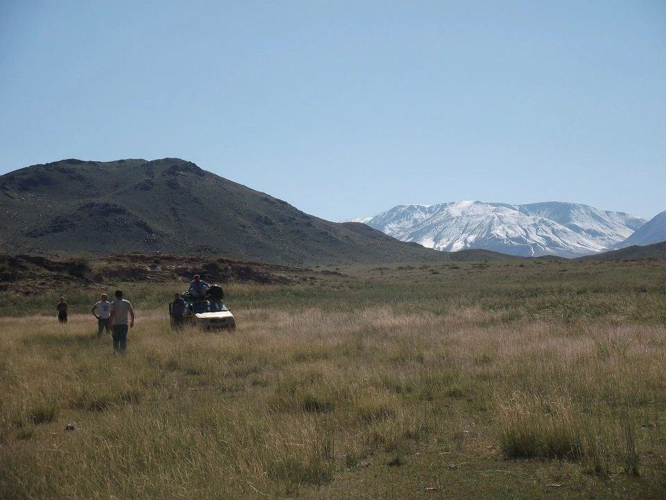 The Mongol Rally car on the steppe with mountains behind