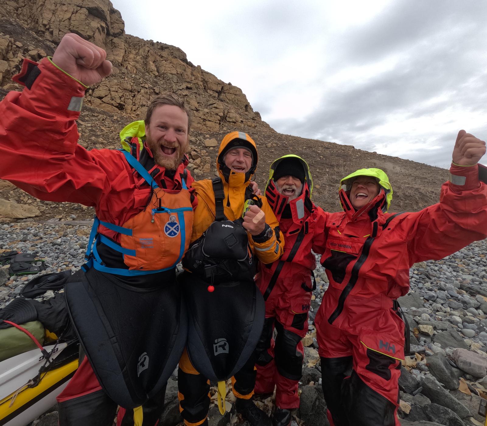 Mark Agnew and his three teammates celebrating on an Arctic shoreline in drysuits